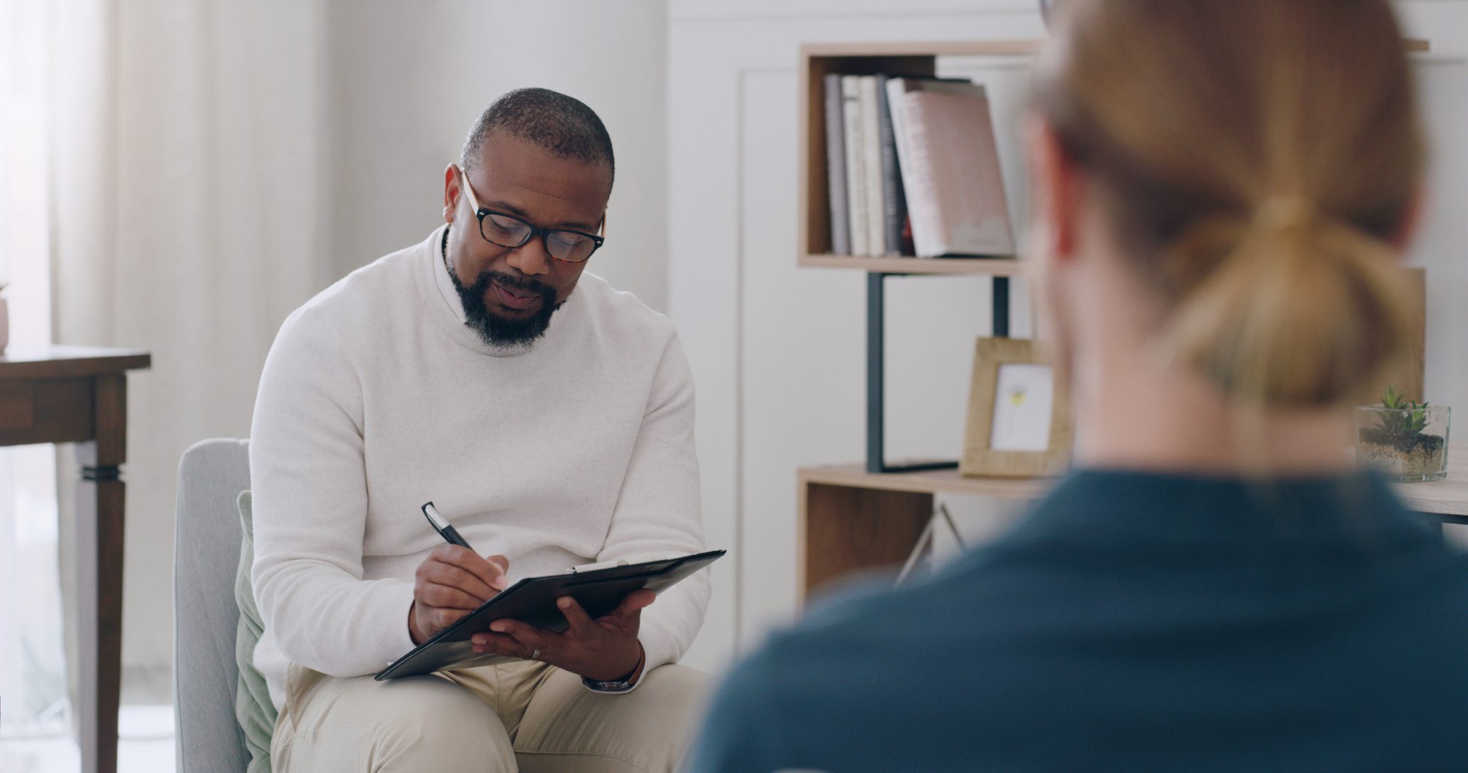 Black man, psychology and writing note with woman patient in counseling appointment for help, support and consulting. Psychologist listening, advice and helping client with mental health or anxiety